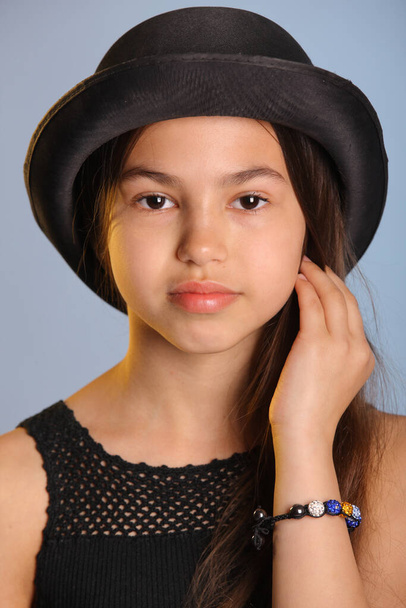 Close-up portrait of a bright cute dark-haired teenage girl 12 years old in a black bowler hat, she looks her brown eyes eye to eye. - Foto, Bild