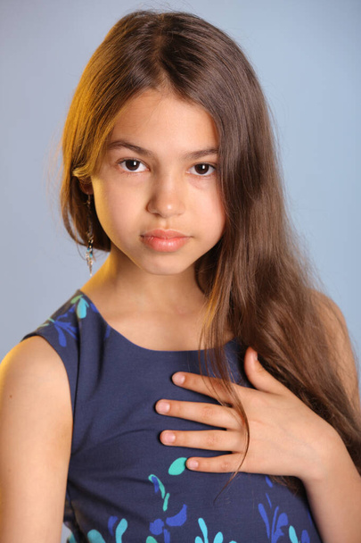 Close-up portrait with hand near face. The portrait shows a beautiful dark-haired teenage girl 12 years old in a blue dress. She looks carefully eye to eye. - Foto, Bild