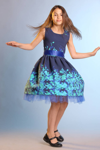 Lovely skinny brunette teenage girl 12 years old in a blue dress is spinning in dance. - Foto, afbeelding