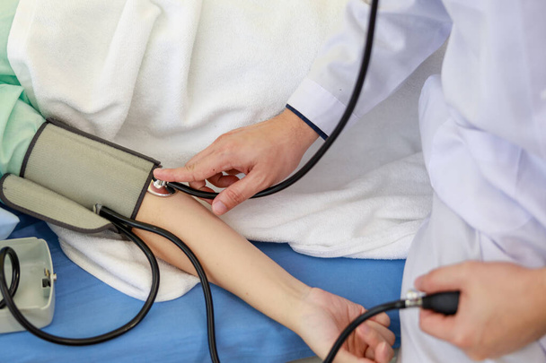 aziatische man arts check up - vrouwelijke patiënt arm uitgebreid op bed  - Foto, afbeelding