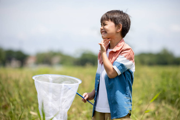 Kleiner Junge jagt Insekten und Schmetterlingen in der Natur grüne Wiese und heiße müde Sonneneinstrahlung  - Foto, Bild