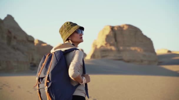 aziatische vrouw met rugzak wandelen in gobi woestijn met yardang landvormen bij zonsondergang - Video