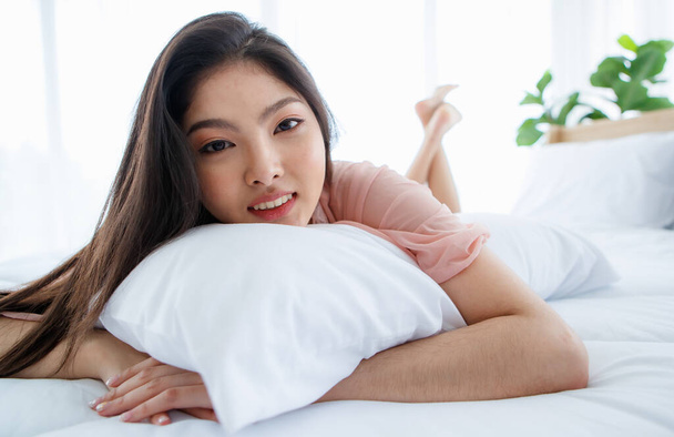 Bela jovem menina sexy impertinente com cabelos longos deitado no travesseiro na cama branca terminam em manhã brilhante e sedutoramente olhando com sorriso para um especial de dia romântico feliz - Foto, Imagem