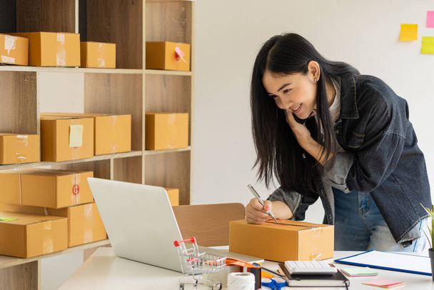 Молодая предпринимательница, работающая дома над онлайн бизнесом Женщины-предприниматели используют ноутбуки, чтобы работать дома и начать бизнес МСП. Маленькие и картонные коробки на рабочем месте - Фото, изображение