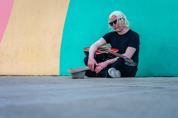 Young albino man with his guitar sitting on the floor resting. Horizontal orientation. Relaxation and inner peace concept. - Fotó, kép