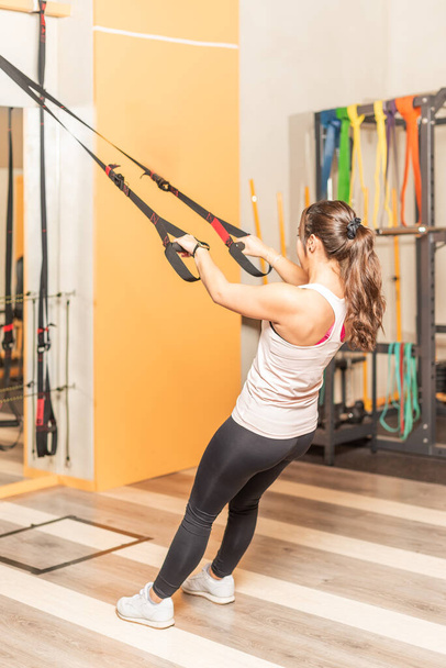 Жінка робить вправи з фітнес-ремінцями в клубі здоров'я
 - Фото, зображення