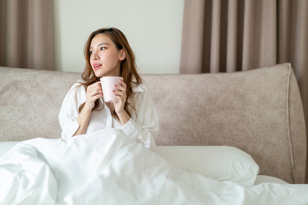 portrait beautiful Asian woman wake up and holding coffee cup or mug on bed in the morning - Φωτογραφία, εικόνα
