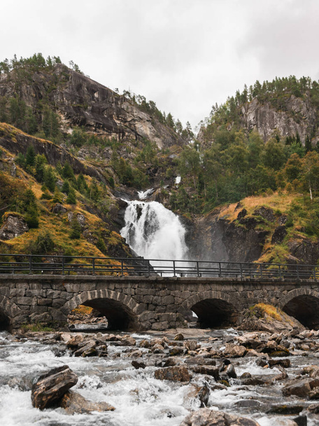 A scenic shot of a bridge in front of the Latefossen waterfall surrounded by mountain forests - Zdjęcie, obraz