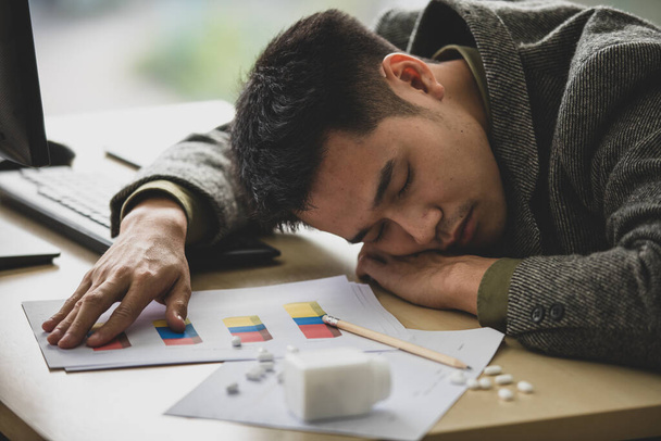 Nuori mies näyttää väsyneeltä. Nukahtaminen paperipinolle töissä päivän aikana, liian paljon vaivaa ja päättäväisyyttä vaikuttaa terveyteen. Mutta torkkuminen voi auttaa keksimään hyviä ideoita sen jälkeen. - Valokuva, kuva