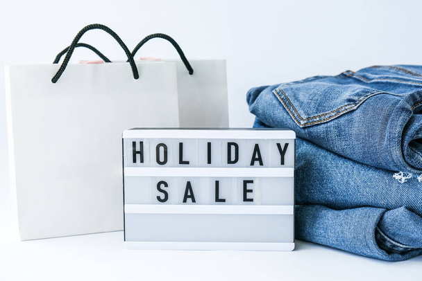 Light board with text HOLIDAY SALE with paper shopping bags, jeans clothes. Big Sale online shopping concept. Promotion advertising. Holiday Cyber monday. - Photo, Image