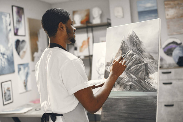 Young African-American artist painting picture in workshop - 写真・画像
