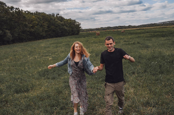 Dwóch młodych mężczyzn i kobiet biegnie wesoło przez pole przeciw stogom siana. jesienny krajobraz natury. podróże lokalne. szczęśliwych związków. zdrowie psychiczne w parze. ukierunkowanie selektywne - Zdjęcie, obraz