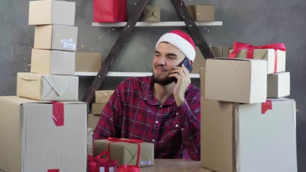 Caucasico maschio piccolo imprenditore si siede a casa ufficio indossando cappello Babbo Natale parlando al telefono. Natale concetto di vendita. - Filmati, video