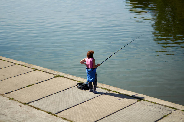 Grandma is fishing on the river embankment - Photo, Image