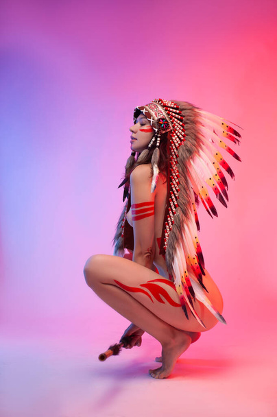 naakt vrouw in native amerikaans kostuum met veren op een neon achtergrond - Foto, afbeelding