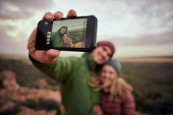 Closeup of male hand holding smartphone taking selfie with girlfriend while on mountain hill after hike - Valokuva, kuva