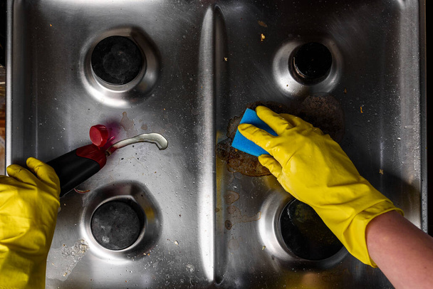 Mano en guantes de goma amarilla limpieza cocina estufa de gas. - Foto, imagen