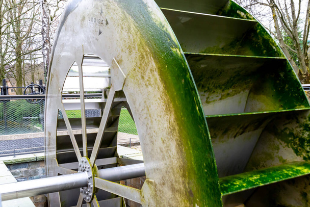 Une roue à eau moderne en métal, sur laquelle les algues vertes ont collé et ne bouge pas actuellement. L'essieu est également en métal - Photo, image