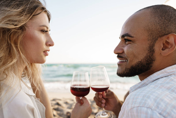 Portrait of a young couple sitting on the beach and drinking wine - Foto, immagini