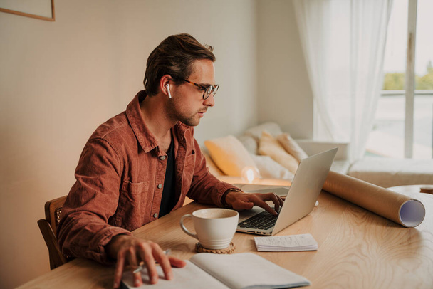 家庭で働く白人男性がノートパソコンでホットコーヒーを飲みながら  - 写真・画像