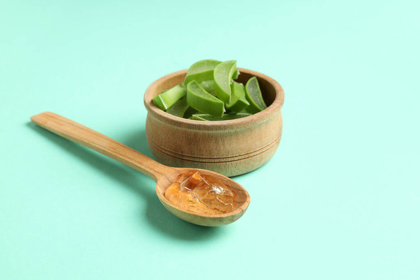 Spoon with aloe gel and bowl with slices on mint background - Photo, Image