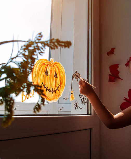 Lapsi maalaus kurpitsa ikkunassa valmistautuu juhlia Halloween. Pieni lapsi kiinnittää sisustaa huoneen sisustuksen paperilepakoilla juhla syksyllä loma kotona Luova perheen vapaa-ajan lukitus uusi todellisuus - Valokuva, kuva