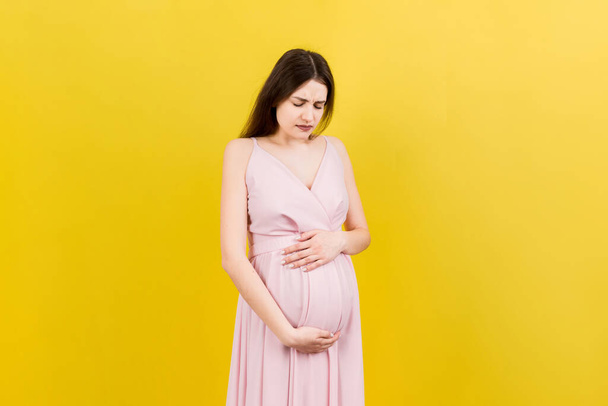 těhotná dívka, která trpí bolestí břicha, stojí na barevném pozadí. izolované. - Fotografie, Obrázek
