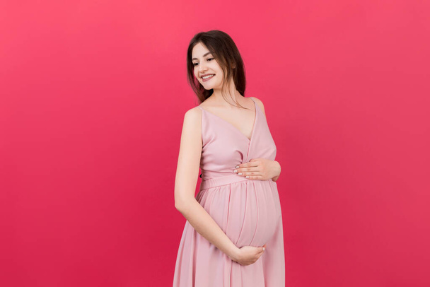 色の背景で彼女の腹部に触れる幸せな妊娠中の女性。未来の母親。赤ん坊を期待してる。スペースのコピー. - 写真・画像