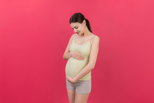 Heureuse femme enceinte touchant son abdomen à fond coloré. La future mère. J'attends un bébé. Espace de copie. - Photo, image