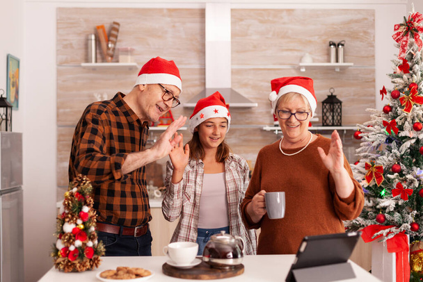 Ευτυχισμένη οικογένεια που φοράει καπέλο Σάντα χαιρετώντας απομακρυσμένους γονείς γιορτάζοντας τα Χριστούγεννα - Φωτογραφία, εικόνα