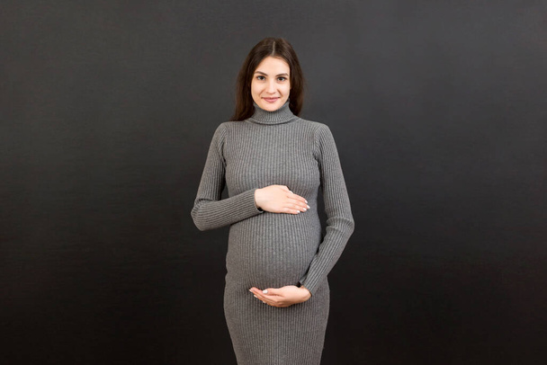 Glückliche schwangere Frau, die ihren Bauch vor farbigem Hintergrund berührt. Die zukünftige Mutter trägt weiße Unterwäsche. Erwartung eines Babys. Kopierraum. - Foto, Bild