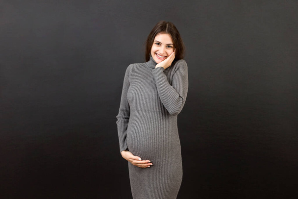 Happy pregnant woman touching her abdomen at Colored background. Future mother is wearing white underwear. Expecting of a baby. Copy space. - Photo, image