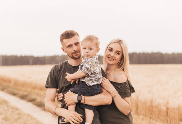 Beautiful family parents and a young son in a wheat field. Mom, Dad and Baby Together. Happy family, parents hugs their little son - Photo, Image