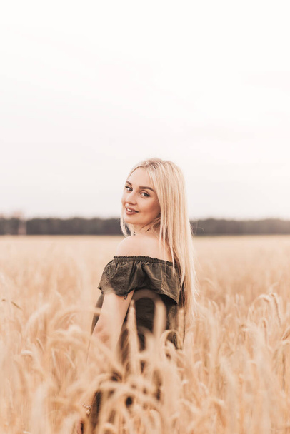 Una joven rubia hermosa con el pelo largo camina a través de un campo de trigo en el verano - Foto, Imagen