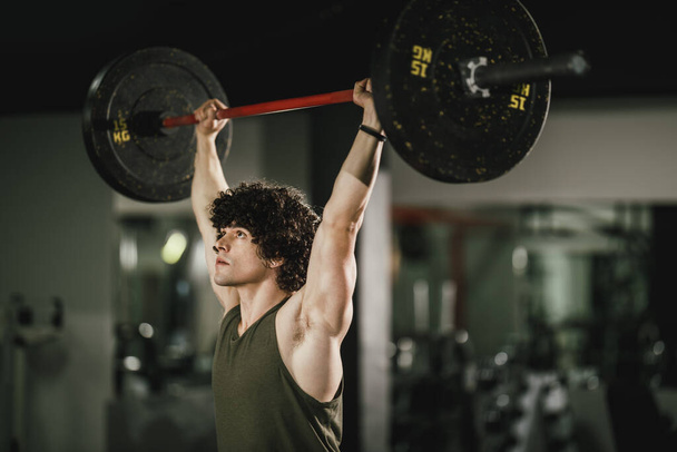 Un joven musculoso está haciendo entrenamiento duro con barra en el gimnasio. - Foto, imagen