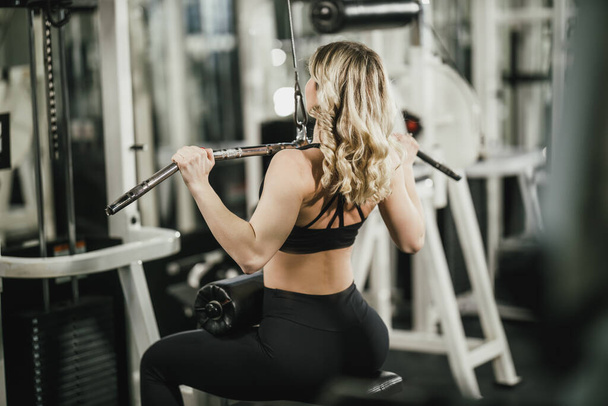 Młoda muskularna kobieta trenuje na maszynie w siłowni. - Zdjęcie, obraz
