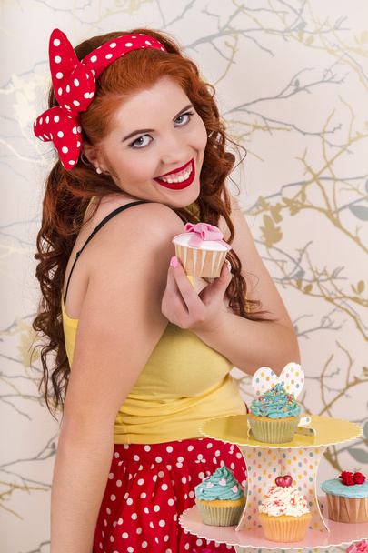 Menina ruiva pinup bonita segurando um cupcake colorido
 - Foto, Imagem