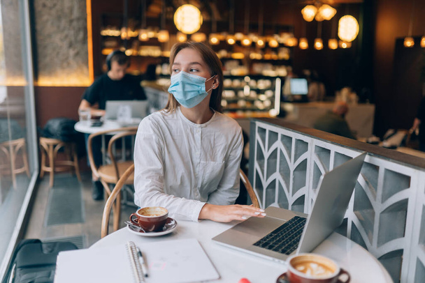 Bella donna che indossa maschera medica, utilizzando il computer portatile per lavorare. - Foto, immagini