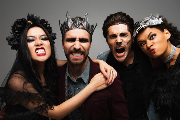 multiethnic friends in scary halloween costumes grimacing at camera isolated on grey - Fotoğraf, Görsel
