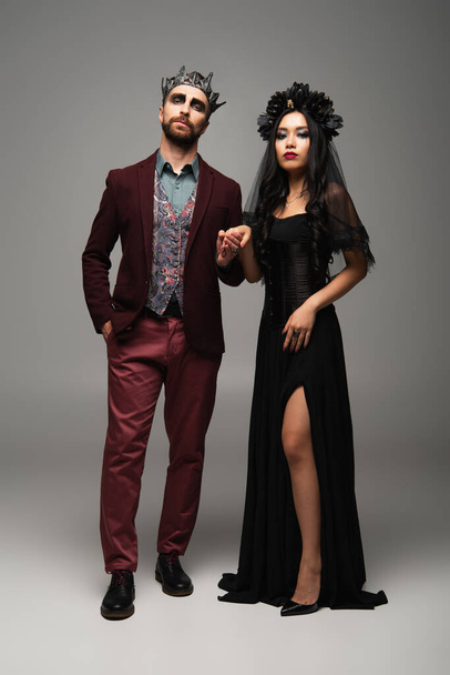 エレガントな異人種間のカップルで吸血鬼ハロウィーンの衣装手を保持しながら立ってグレー - 写真・画像