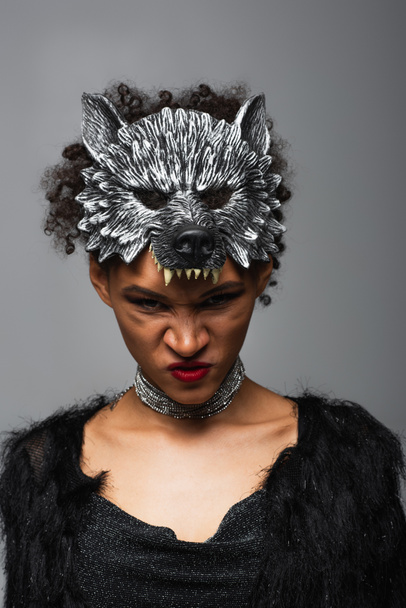 angry african american woman in werewolf halloween mask frowning at camera isolated on grey - Foto, Imagen