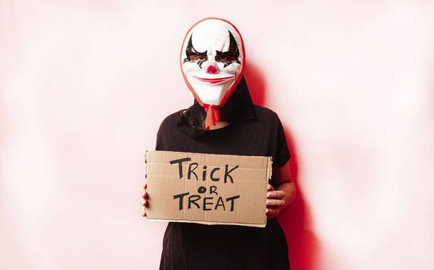 Žena s halloween maskou drží nápis s frází léčbě nebo trik na barevném pozadí. Halloween koncept. - Fotografie, Obrázek