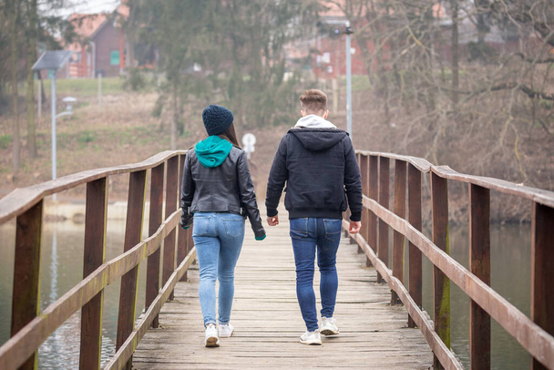若いカップルは、ハンガリーのZalaegerszegのGebart湖で霧の多い冬の日に古い木製の橋を歩いています - 写真・画像