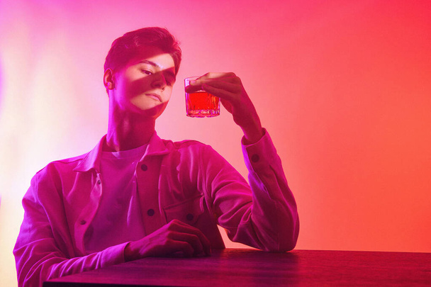 Человек на оранжево-фиолетовом фоне с бокалом виски - Фото, изображение