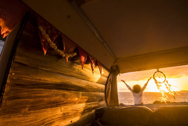 Вид ззаду на жінку з обіймами, витягнутими захоплюючим мальовничим морським пейзажем під час заходу сонника, що звисає з фургона
. - Фото, зображення