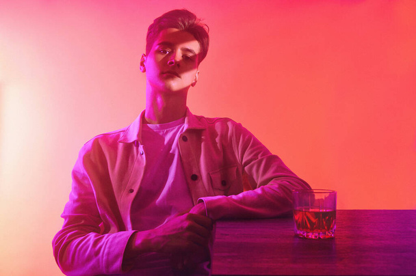 Een man op een oranje-paarse achtergrond met een glas whisky - Foto, afbeelding