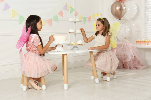 Cute little girls wearing fairy costumes at table with desserts in decorated room - Fotografie, Obrázek