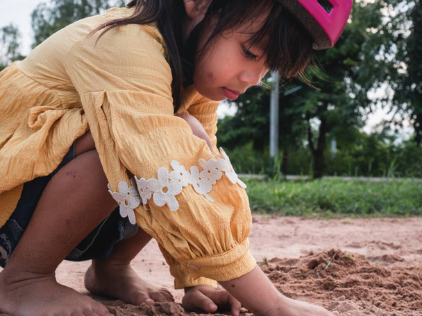 Roztomilé děvčátko v helmách si hraje s pískem v parku za slunečného letního dne, dává si pauzu po cyklistickém tréninku. rozvíjet představivost a průzkum. - Fotografie, Obrázek