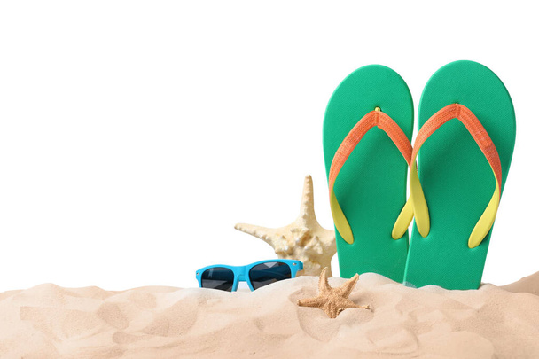 Green flip flops, starfishes and sunglasses on sand against white background - Photo, image