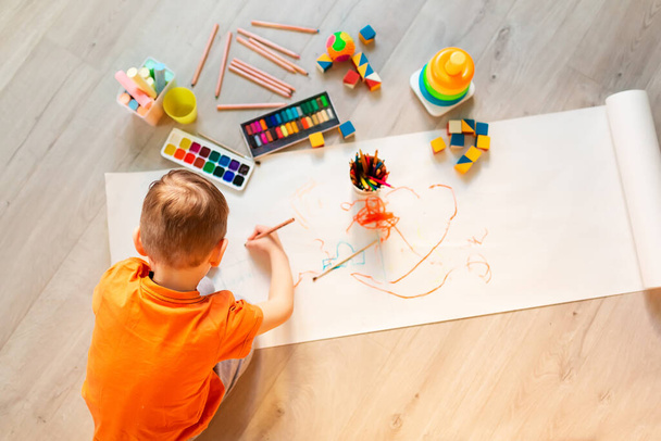 Egy kisfiú rajzolt egy képet a padlón a szobájában, felülnézetből. A gyermekek művészete és kreativitása - Fotó, kép